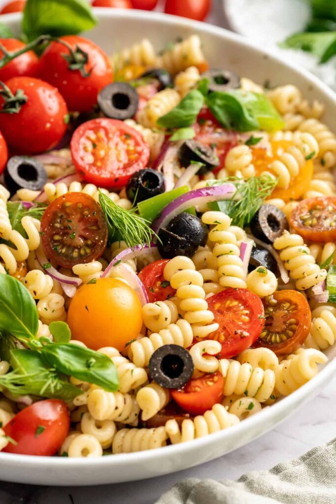 Insalata di pasta fredda vegana con pomodorini colorati, olive nere, cipolla rossa e basilico fresco