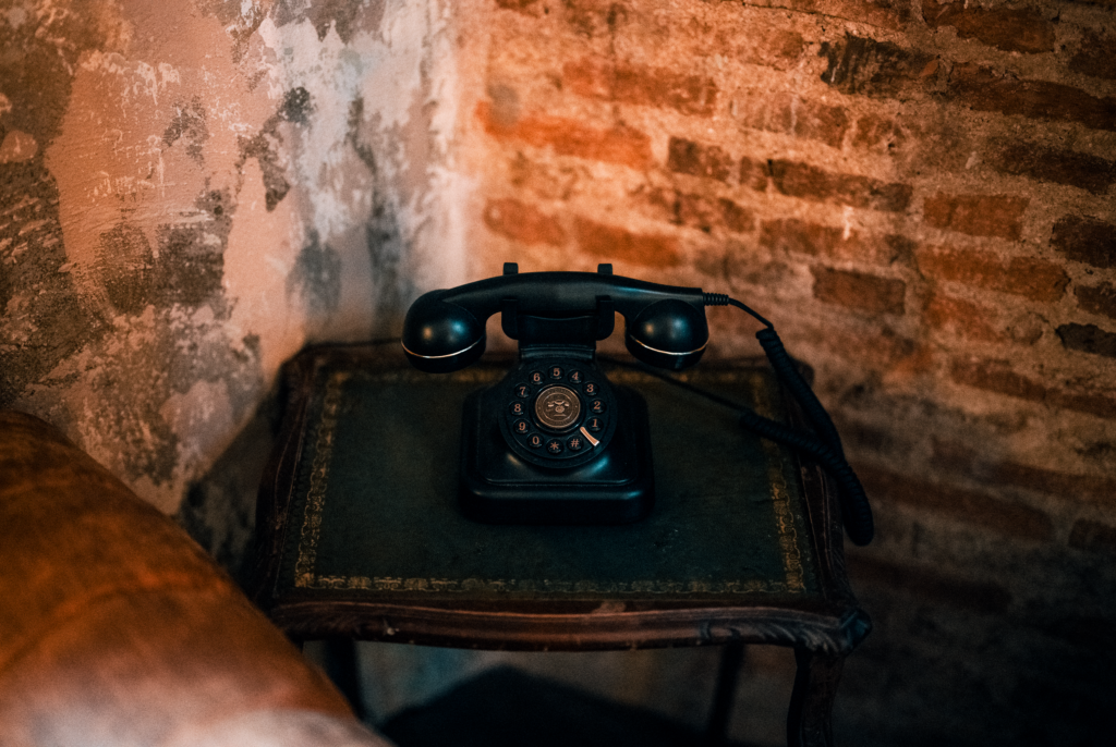 A classic black rotary telephone sits on an antique table by a brick wall, evoking nostalgia.