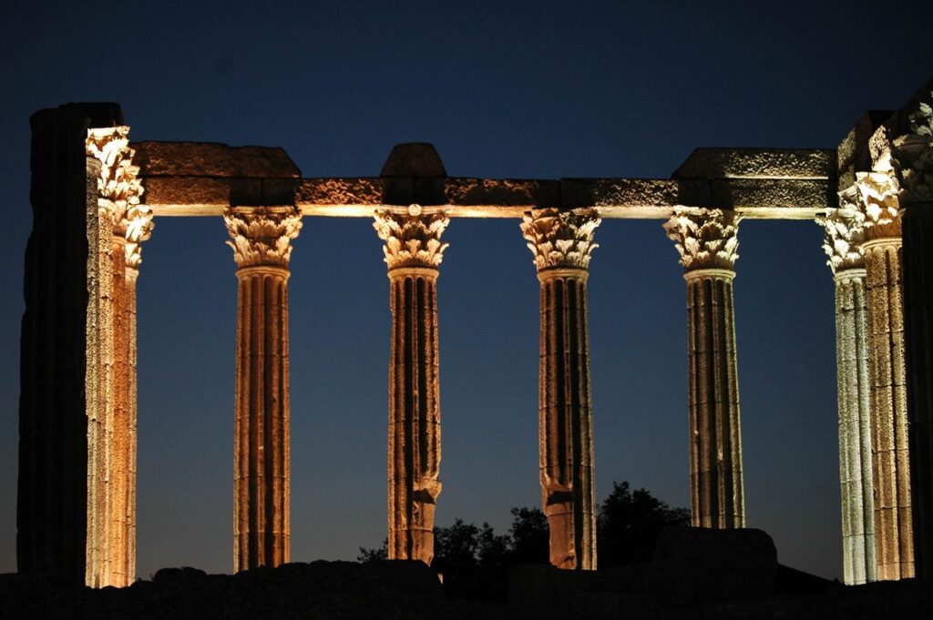 Columns of an ancient Greek or Roman temple illuminated against the night sky.